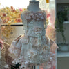 Delicate lace dress on a mannequin with floral embellishments in a softly blurred indoor setting.