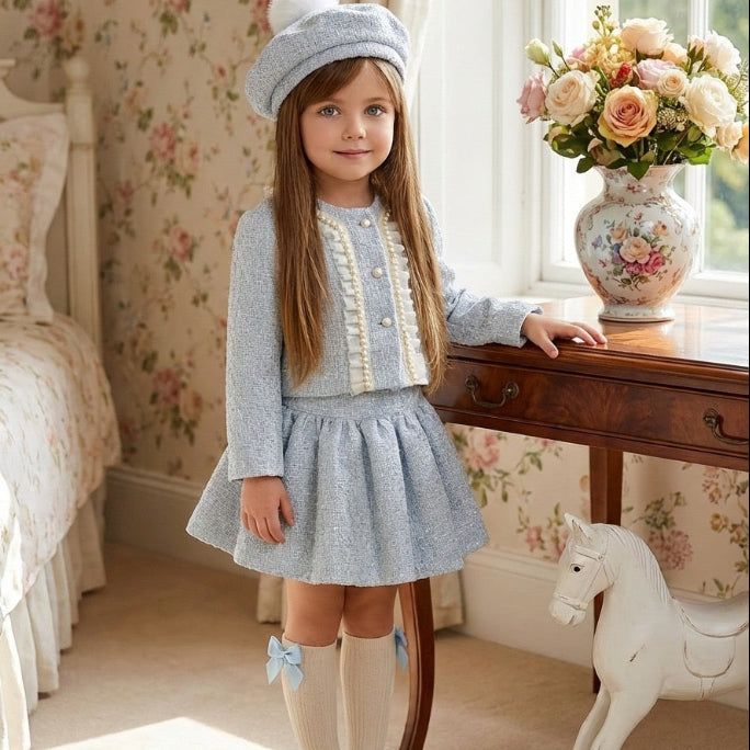 Young girl in a light blue dress and hat standing in a room with floral wallpaper and a rocking horse.
