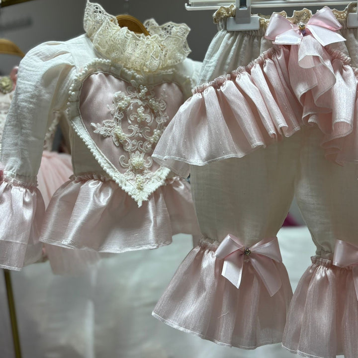 Delicate pink and white dress with lace details on a hanger.