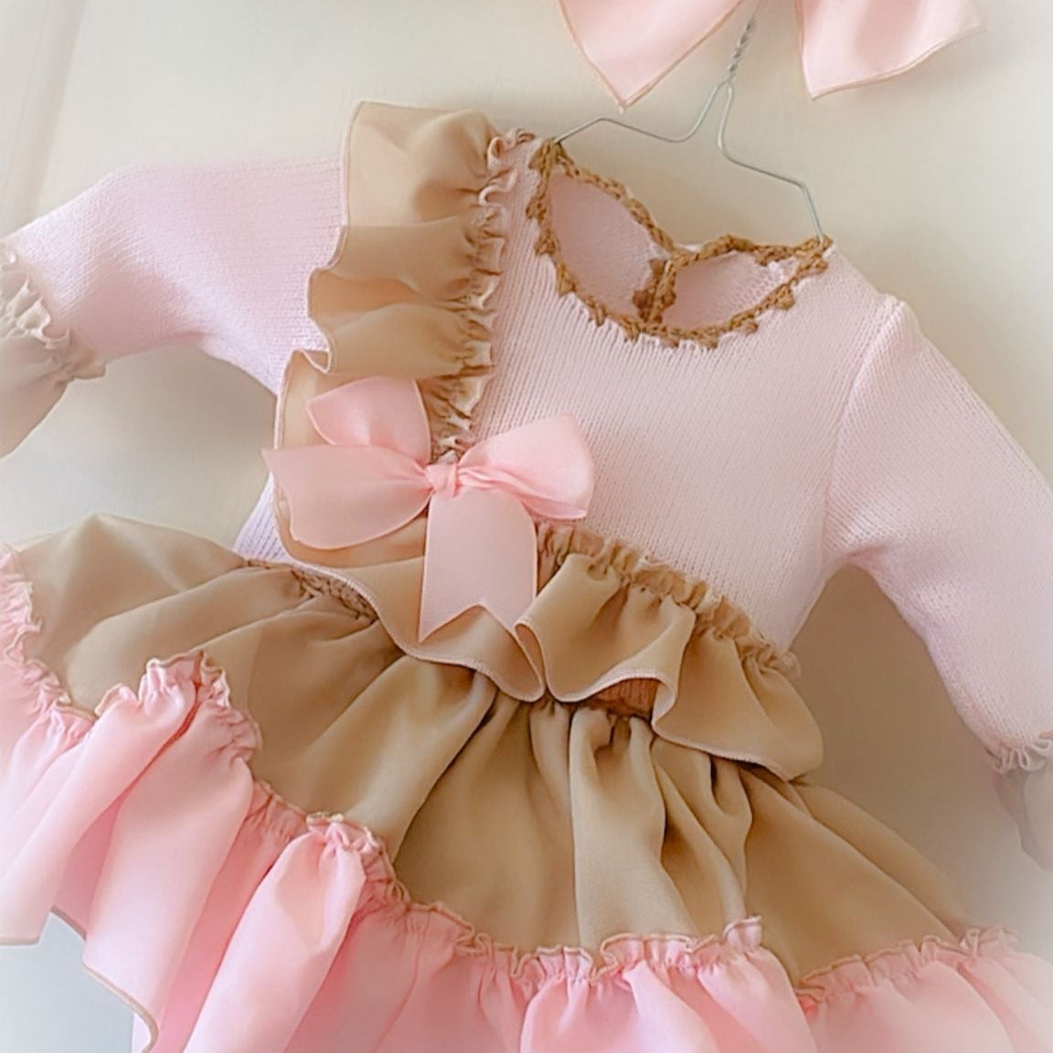 Pink and beige baby outfit with ruffles and bows on a light background