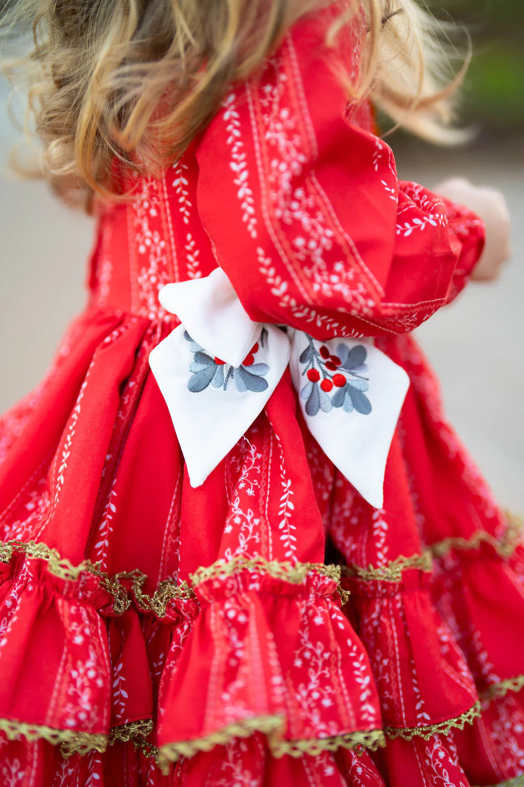 Red dress with white embroidery and a decorative bow worn by a child.