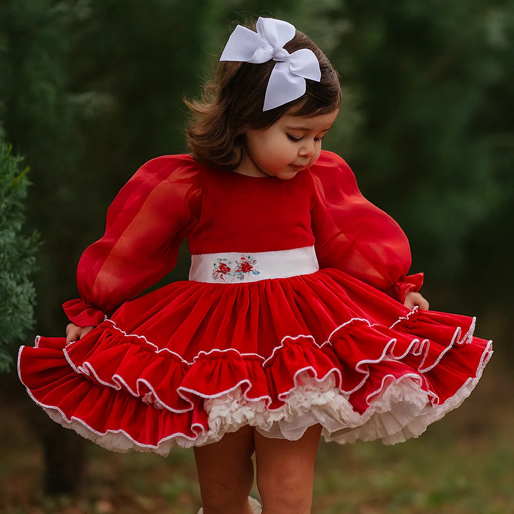 Young girl in a red dress with white trim and white boots standing outdoors.